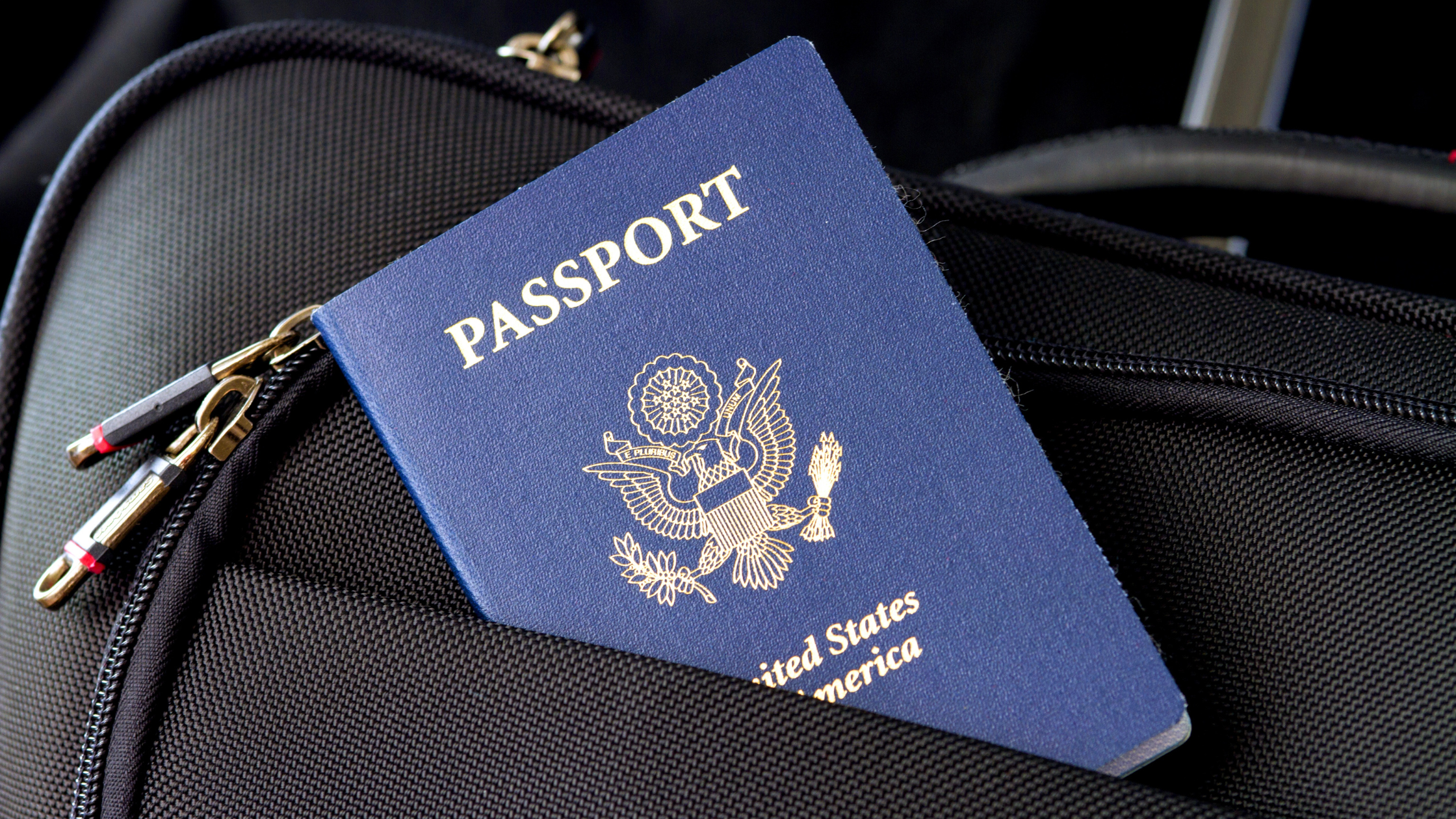 Photograph showing a United States passport tucked into the side pocket of a black airplane carry-on bag.